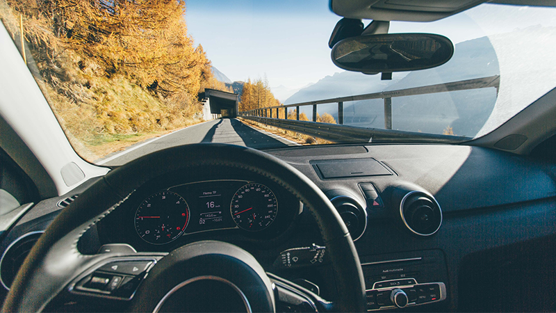 pexels-riccardo-bresciani-228094_800x450 a view from the driver's seat looking past the steering wheel at a mountain landscape around the road